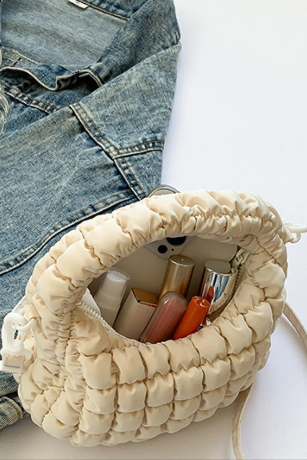 Padded crescent crossbody bag in ivory with sculptural texture, holding makeup and a phone.