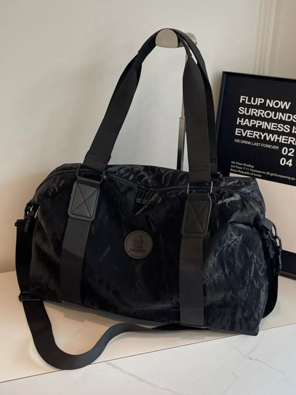 Black medium oxford cloth travel bag with adjustable strap and round logo detail.