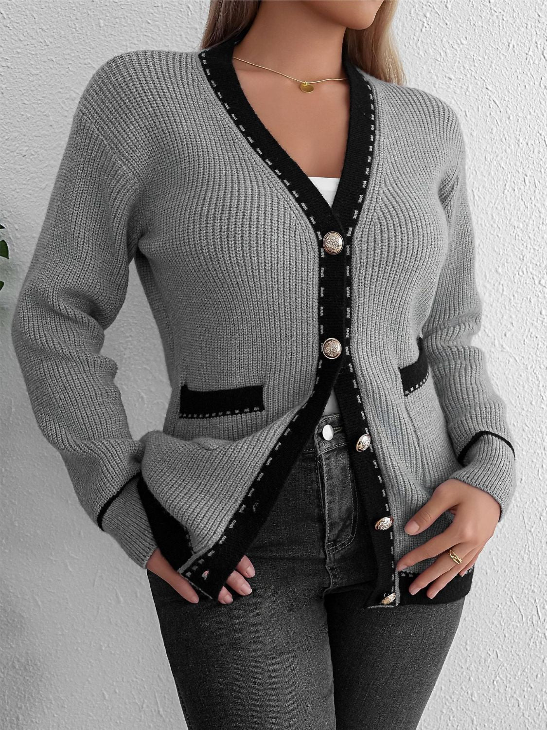 Gray knit cardigan with black contrast trim and gold buttons, featuring patch pockets.