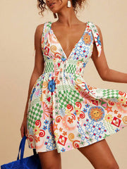 Playful printed mini dress with tied straps, V-neck, smocked waist, and colorful sun and checkered patterns.