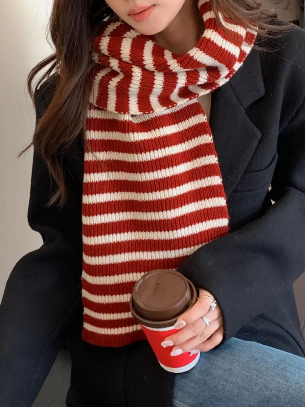 Cozy wool striped winter scarf in deep red and white, worn by a woman holding a coffee cup.