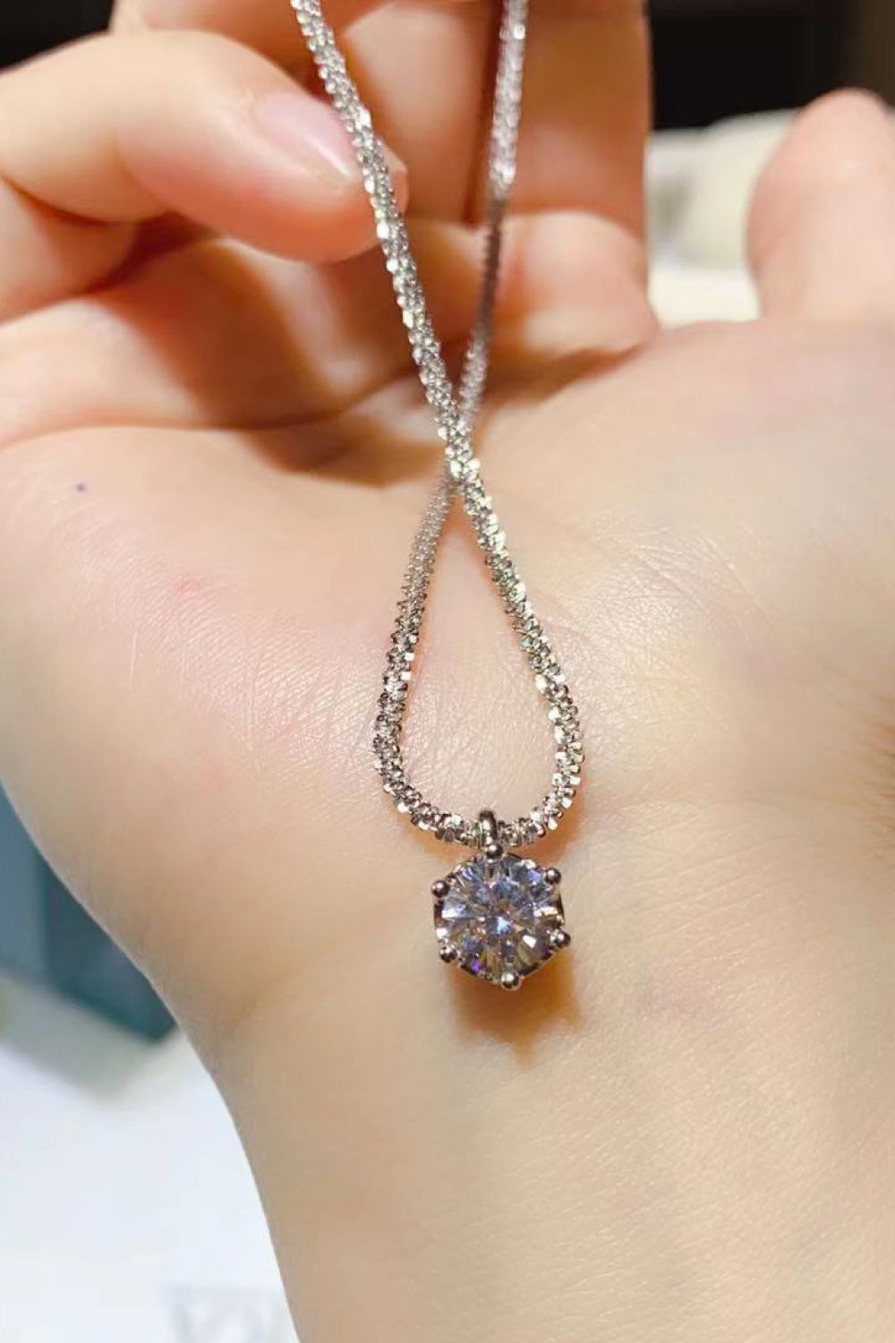 Silver pendant necklace with a round moissanite stone on a textured chain.
