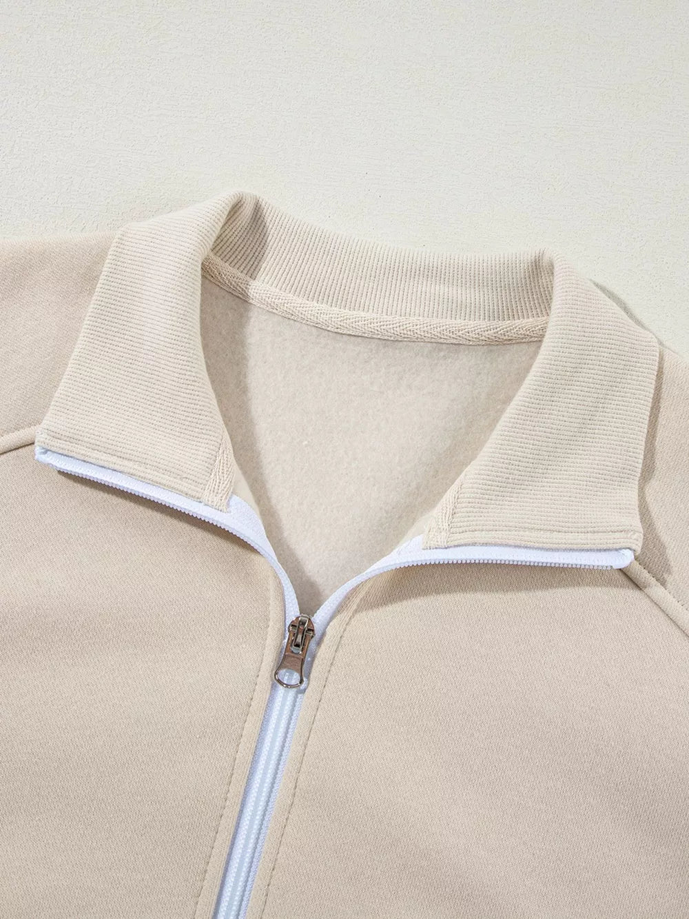 Beige cotton zip-up jacket with ribbed collar and white zipper detail.