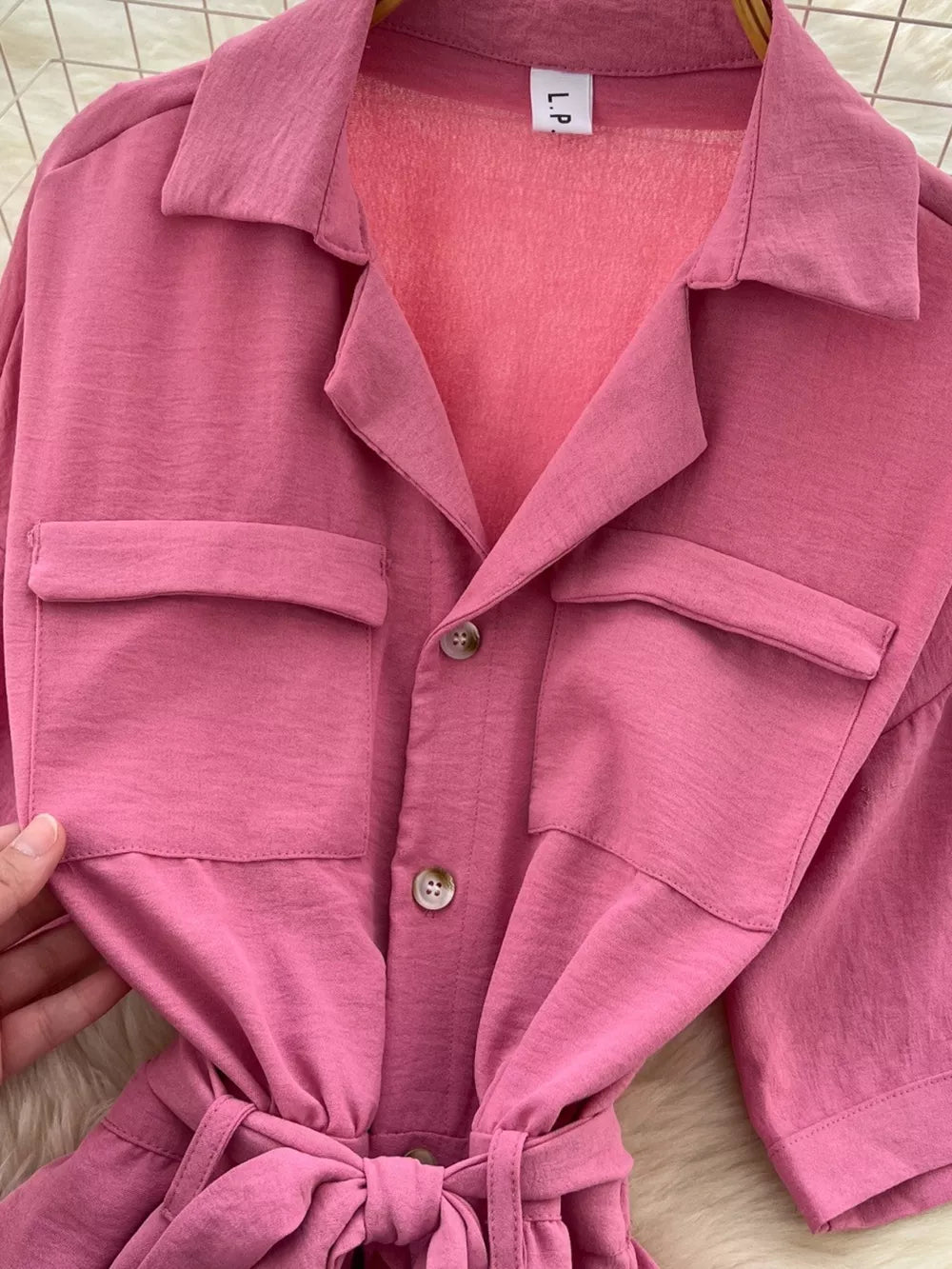 Pink belted wide-leg maternity jumpsuit with buttoned pockets and tie waist.