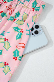 Blush pink pajama pants with holly print and a side pocket holding a phone.