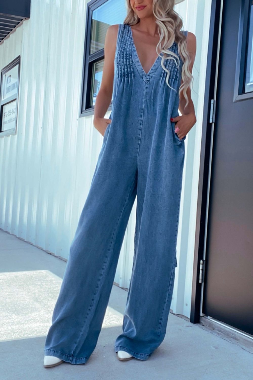 Medium wash denim jumpsuit with pleated bodice and wide-leg pants.