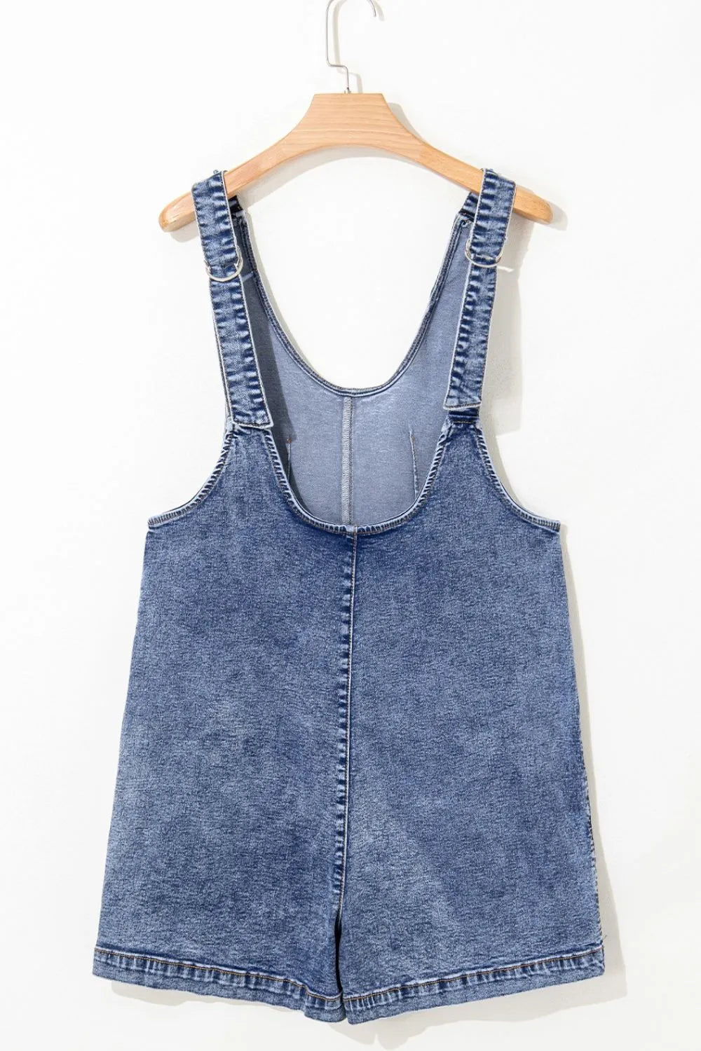 Acid wash denim romper with patch pockets and adjustable straps.