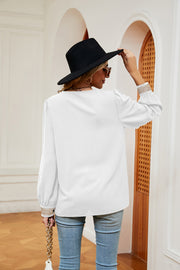 White blouson top with embroidered trim on cuffs and subtle vertical ribbing.