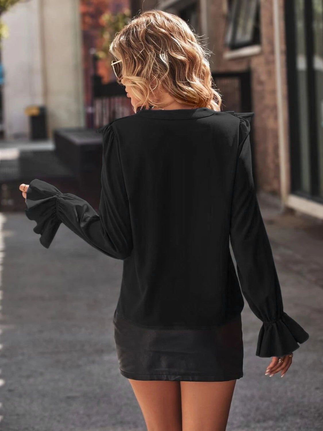 Black polyester blouse with ruffled shoulders and bell sleeves.