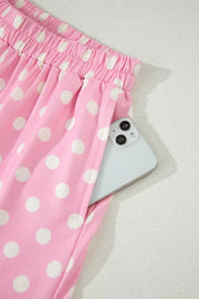 Pink polka dot polyester shorts with pockets and elastic waist, phone visible in pocket.