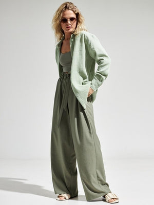 Light green textured cotton overshirt with relaxed fit and button front, styled with wide-leg pants.