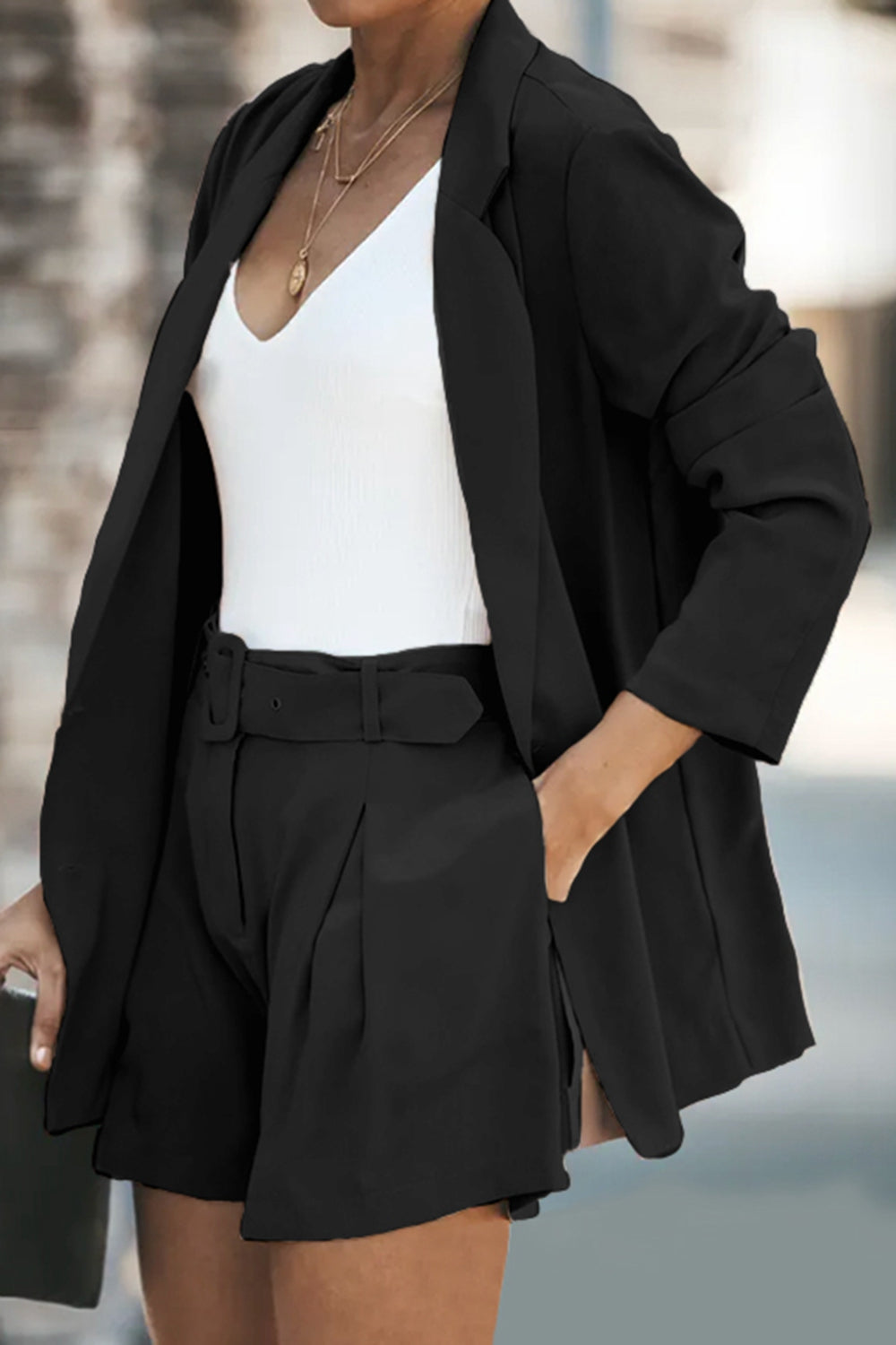 Black double-breasted blazer and belted pleated shorts set with a white V-neck top.