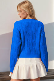 Blue cable knit sweater with crew neck and long sleeves, detailed with a bow embellishment.