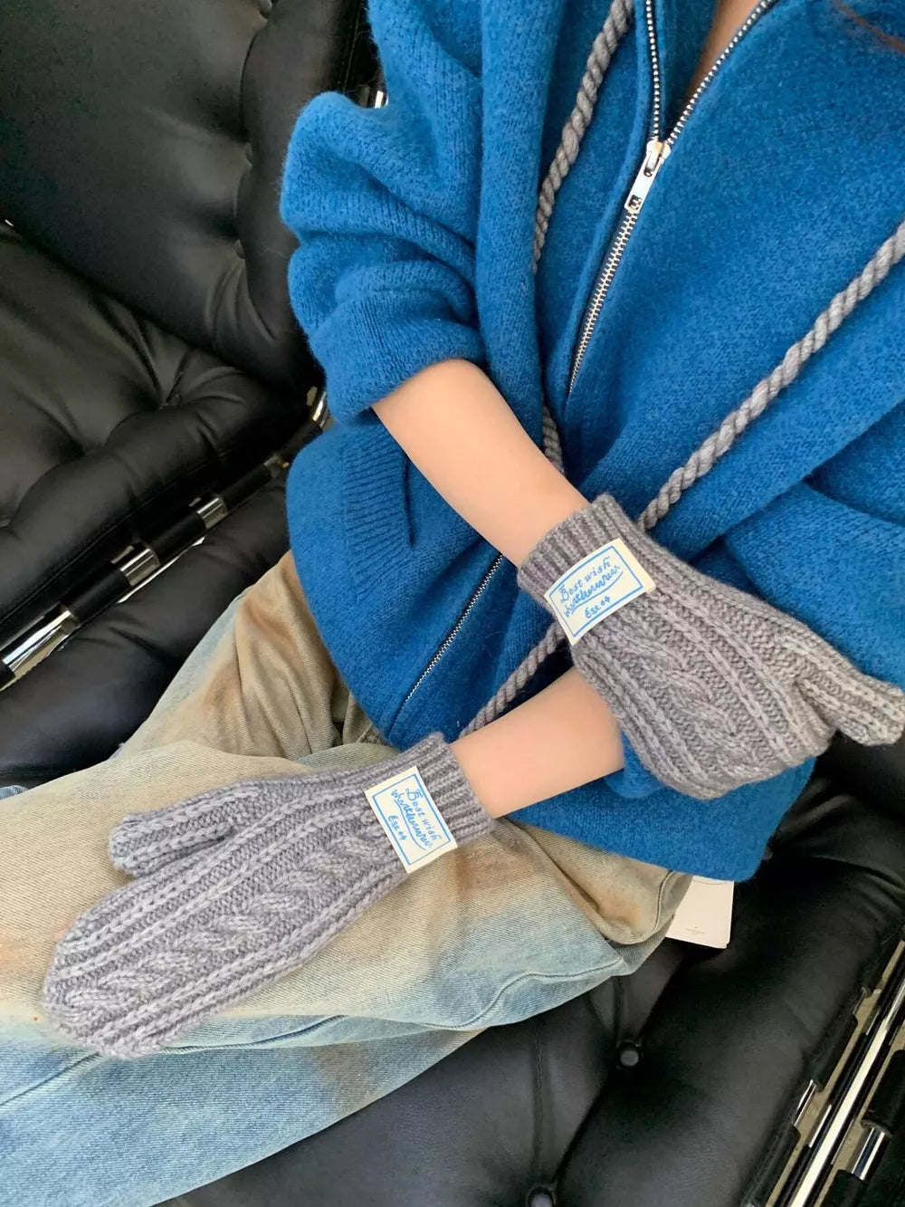 Gray cable knit acrylic mittens with braided detail and white tags.