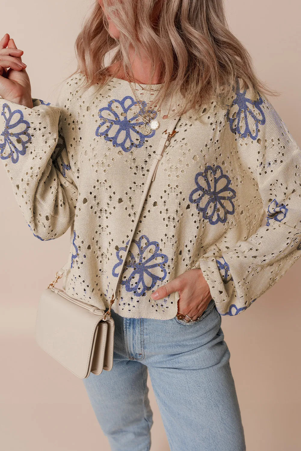 Beige knit pullover with blue floral embroidery and eyelet details.