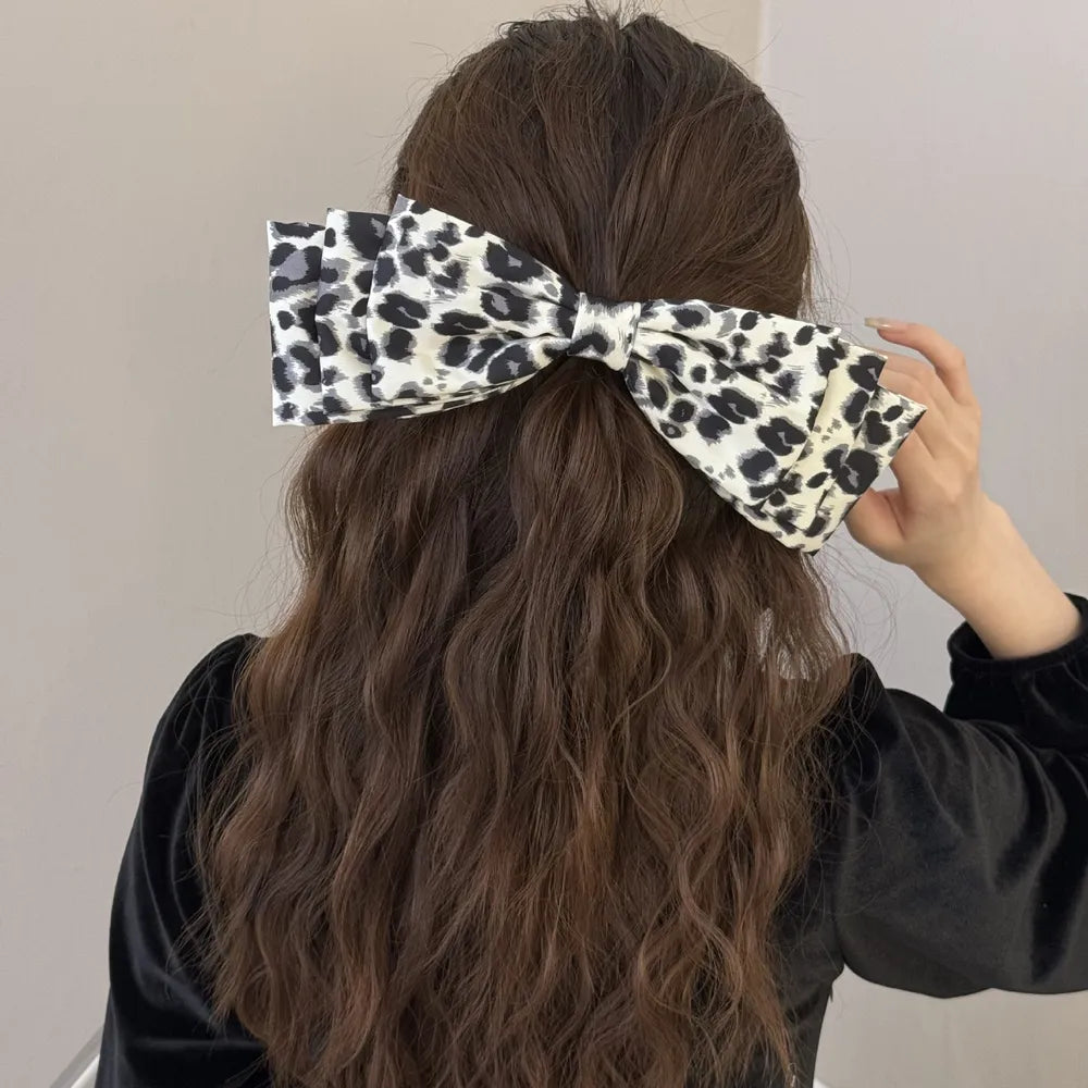 Oversized leopard print hair bow with layered fabric detail, worn in long brown hair.
