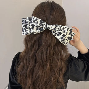 Oversized leopard print hair bow with layered fabric detail, worn in long brown hair.