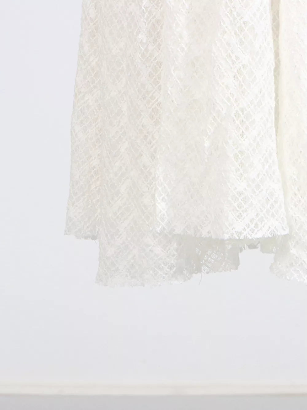 White lace maxi dress with a textured diamond pattern and ruffled hem detail.