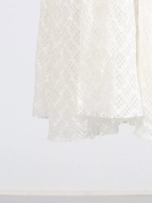White lace maxi dress with a textured diamond pattern and ruffled hem detail.