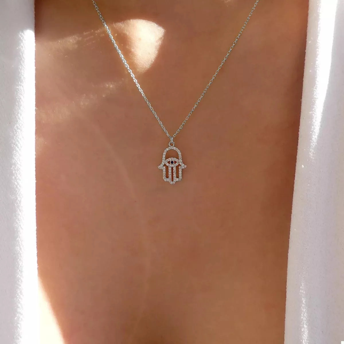Silver Evil Eye Hamsa necklace with rhinestone details.