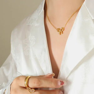 Delicate gold bow pendant necklace on a fine chain, styled with a white satin shirt.