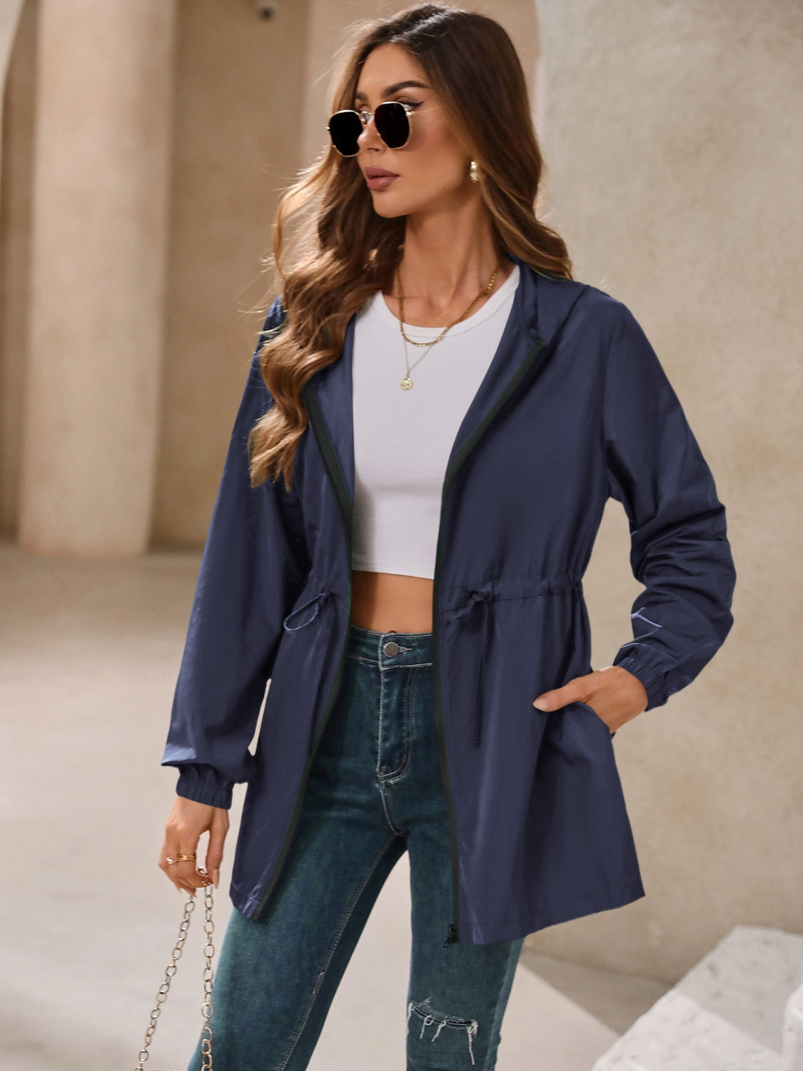 Navy hooded jacket with cinched waistline and zip front, styled with jeans.