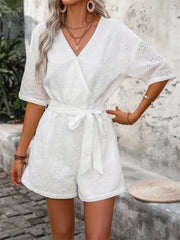 White eyelet romper with V-neck, short sleeves, and tie waist detail.