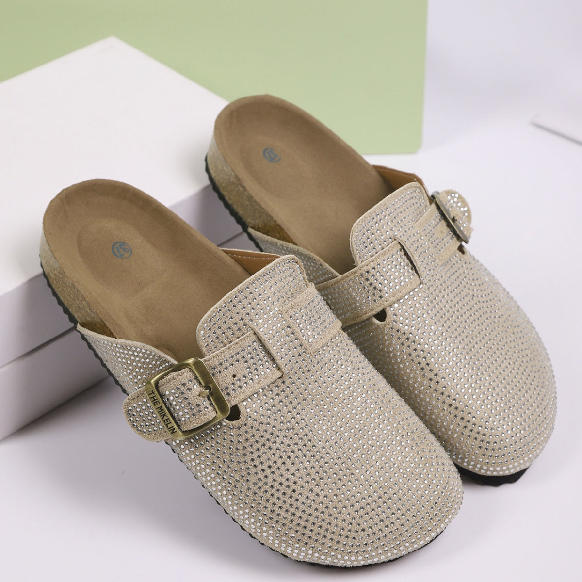 Khaki rhinestone buckle slip-on mules with cork sole and adjustable strap.