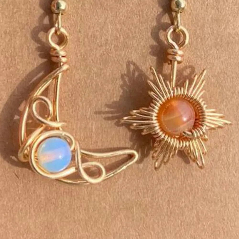Gold celestial asymmetrical drop earrings with moon and sun charms and gemstone accents.