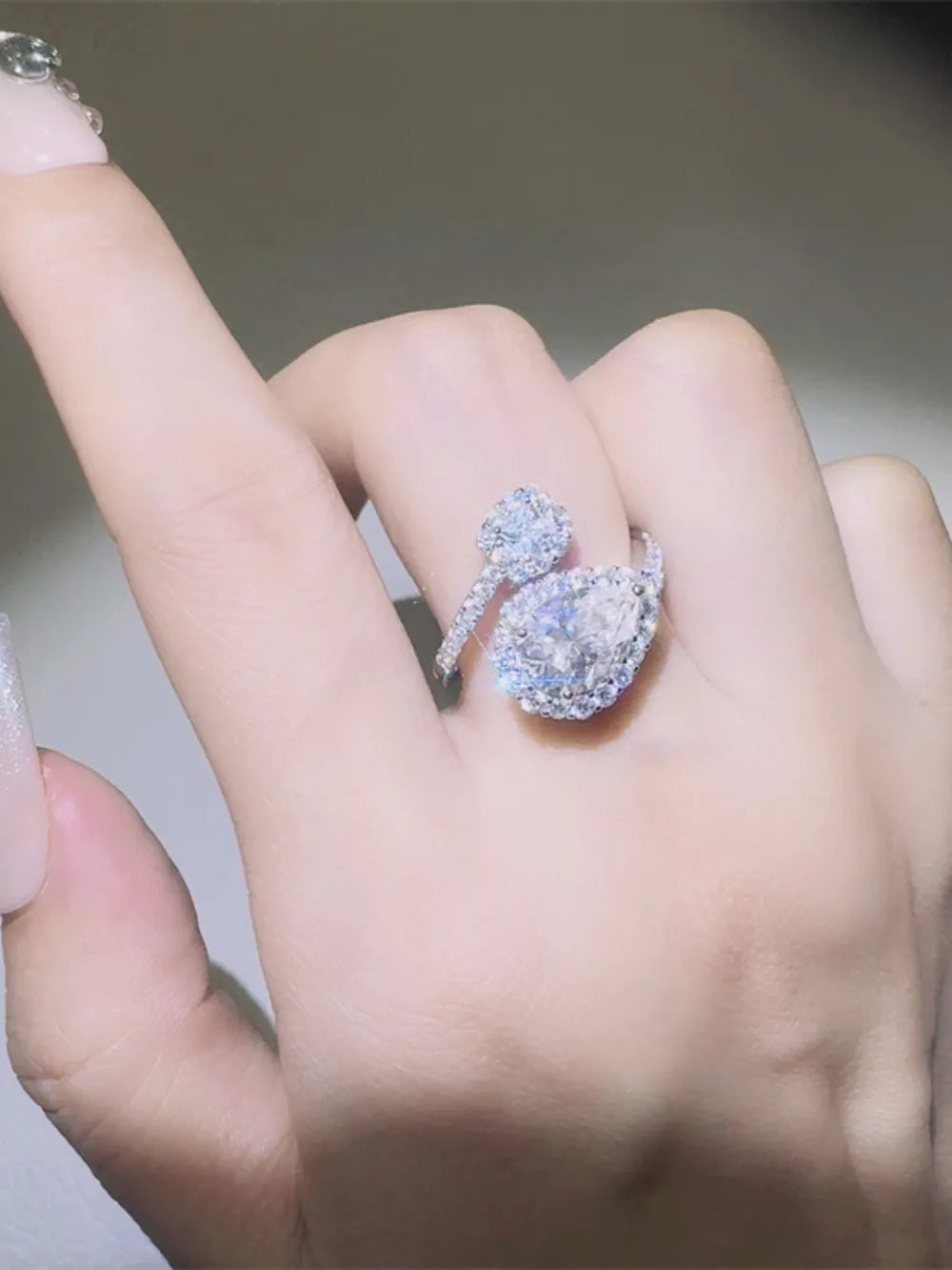 Silver bypass ring with halo and pear-shaped center stone, adorned with small diamonds.