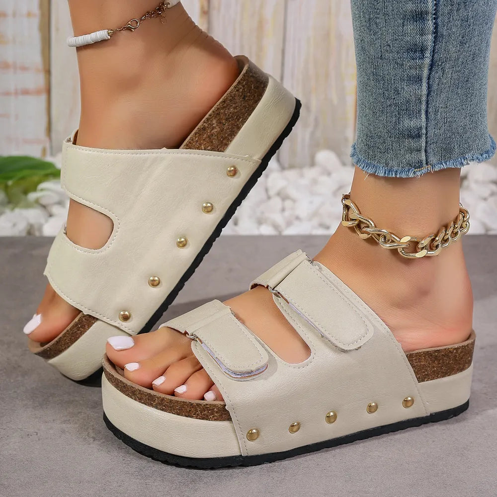 Beige platform sandals with double buckle straps and gold stud details.