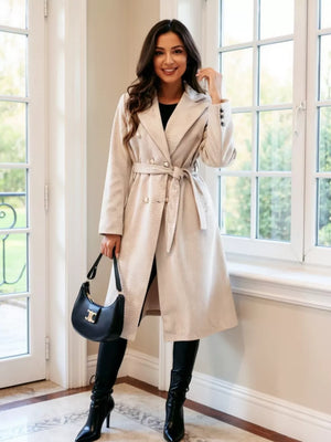Apricot tailored double-breasted trench coat with waist tie and button details.