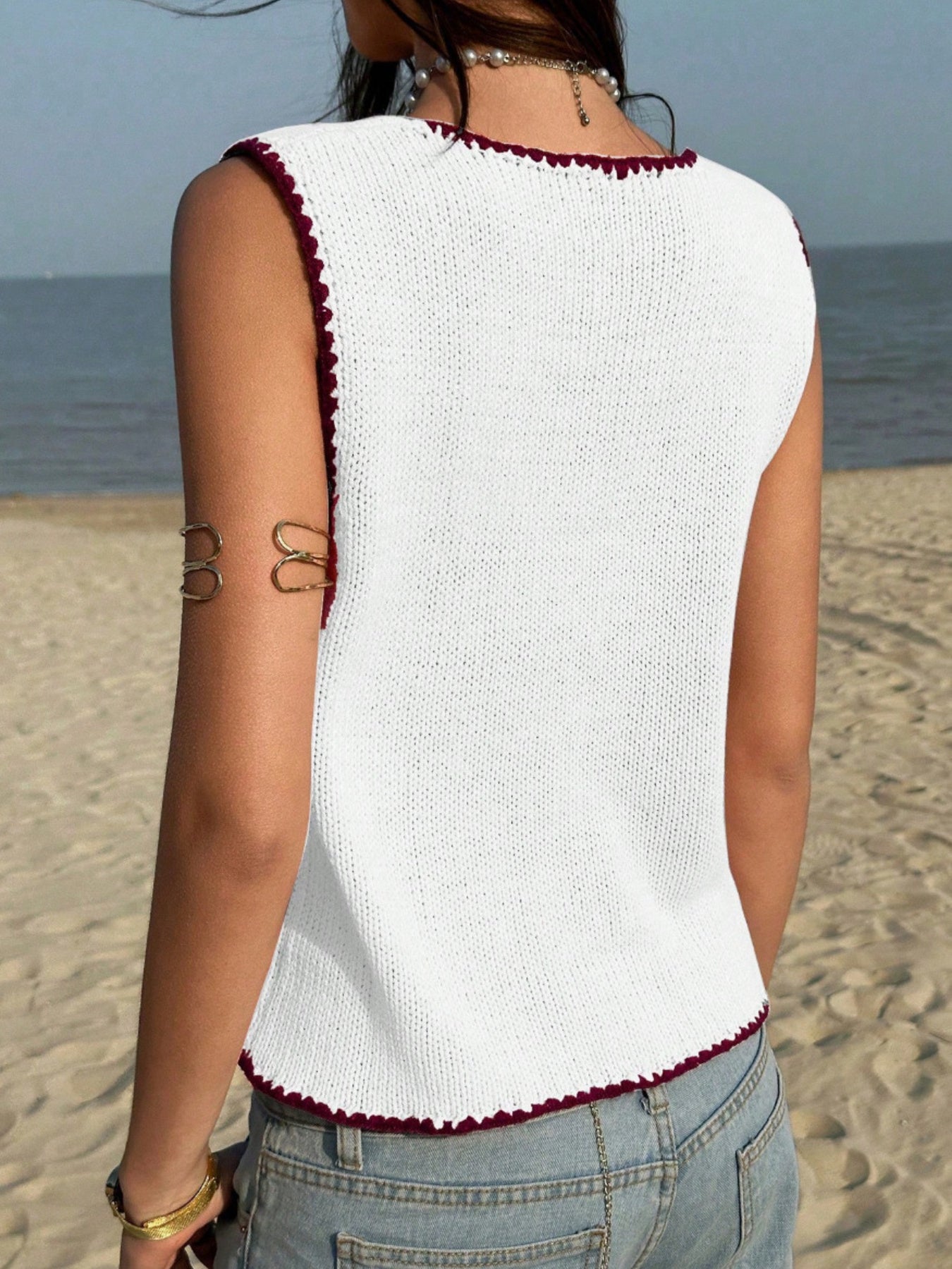 White knit sweater vest with dark red trim and scalloped hem.