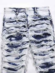 Distressed shredded denim jeans in medium wash with artistic sculptural detailing.