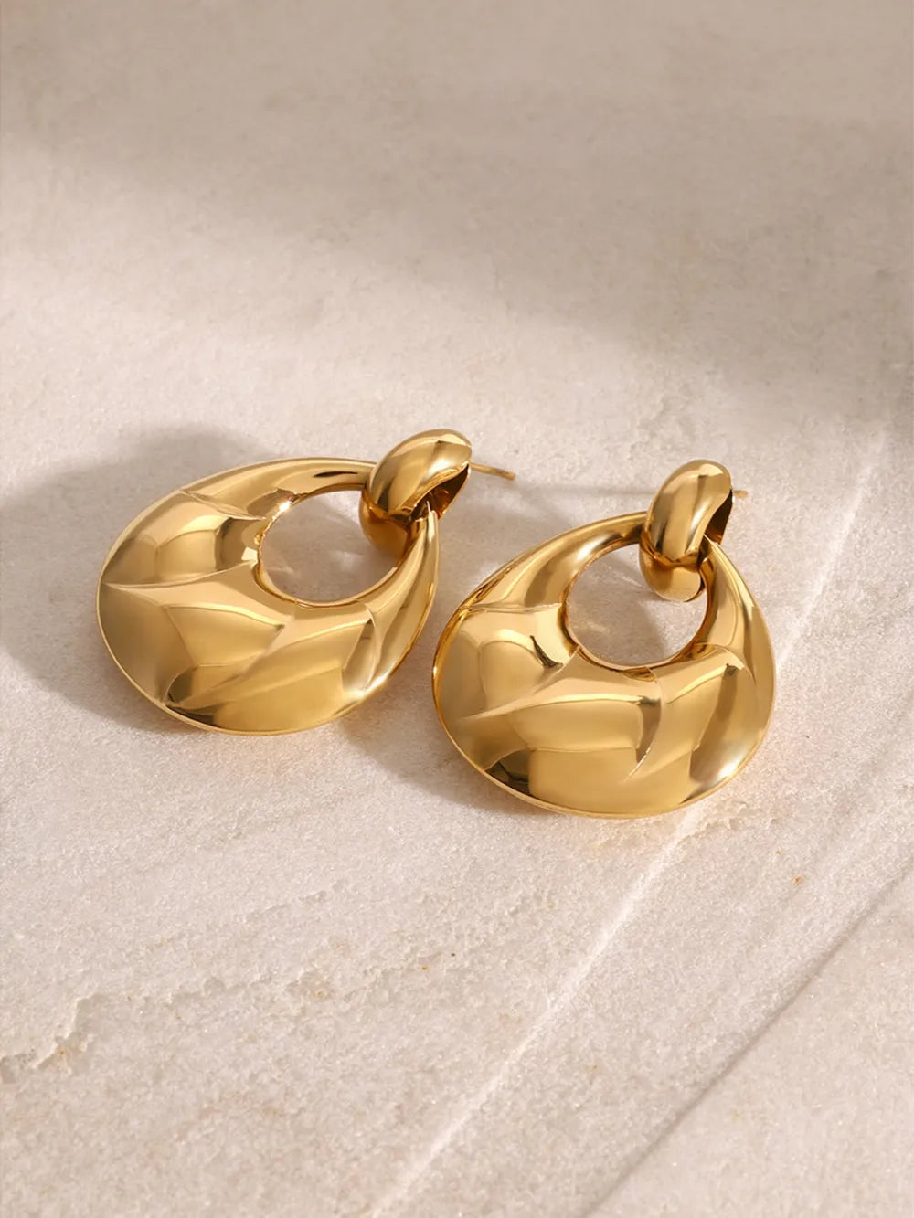Gold statement earrings with sculpted, textured surface and open teardrop shape.