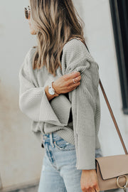 Gray textured knit sweater with bell sleeves and side slits, styled with jeans.