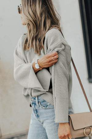 Gray textured knit sweater with bell sleeves and side slits, styled with jeans.