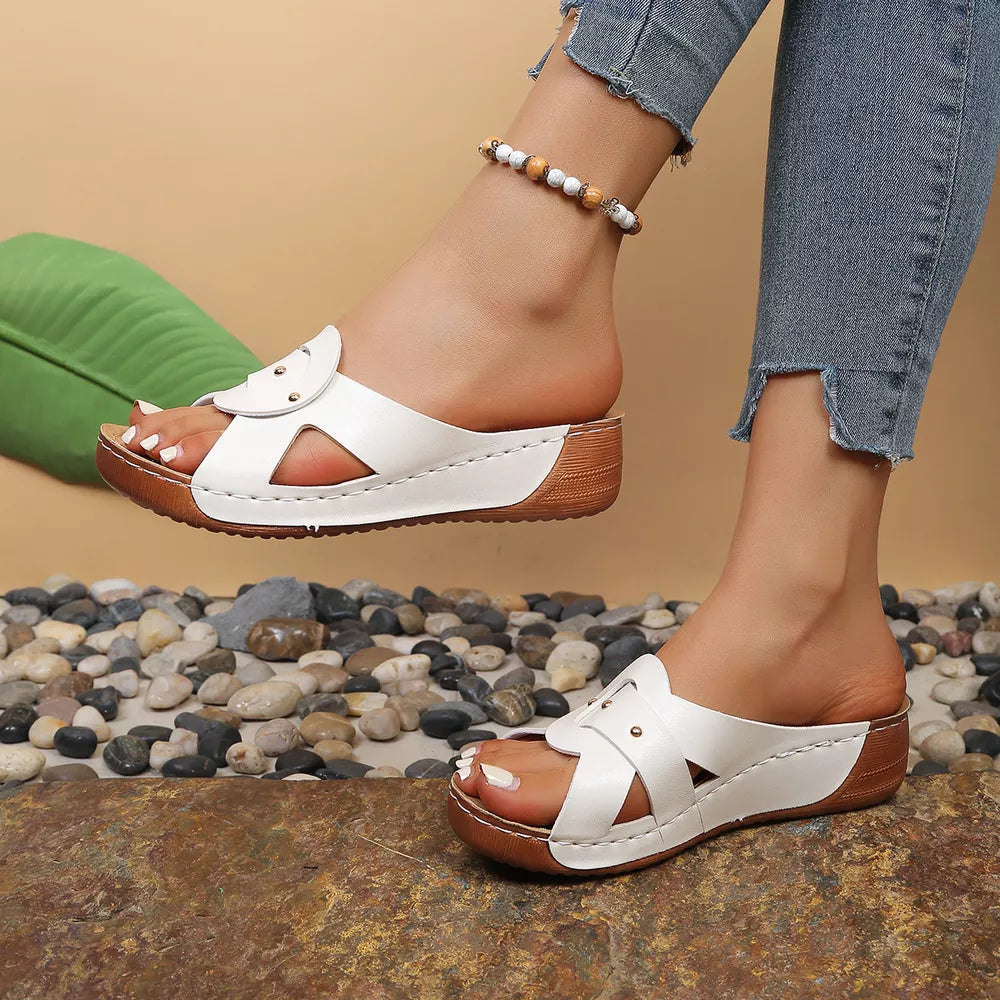 White embellished open-toe wedge sandals with decorative straps and a wooden heel.