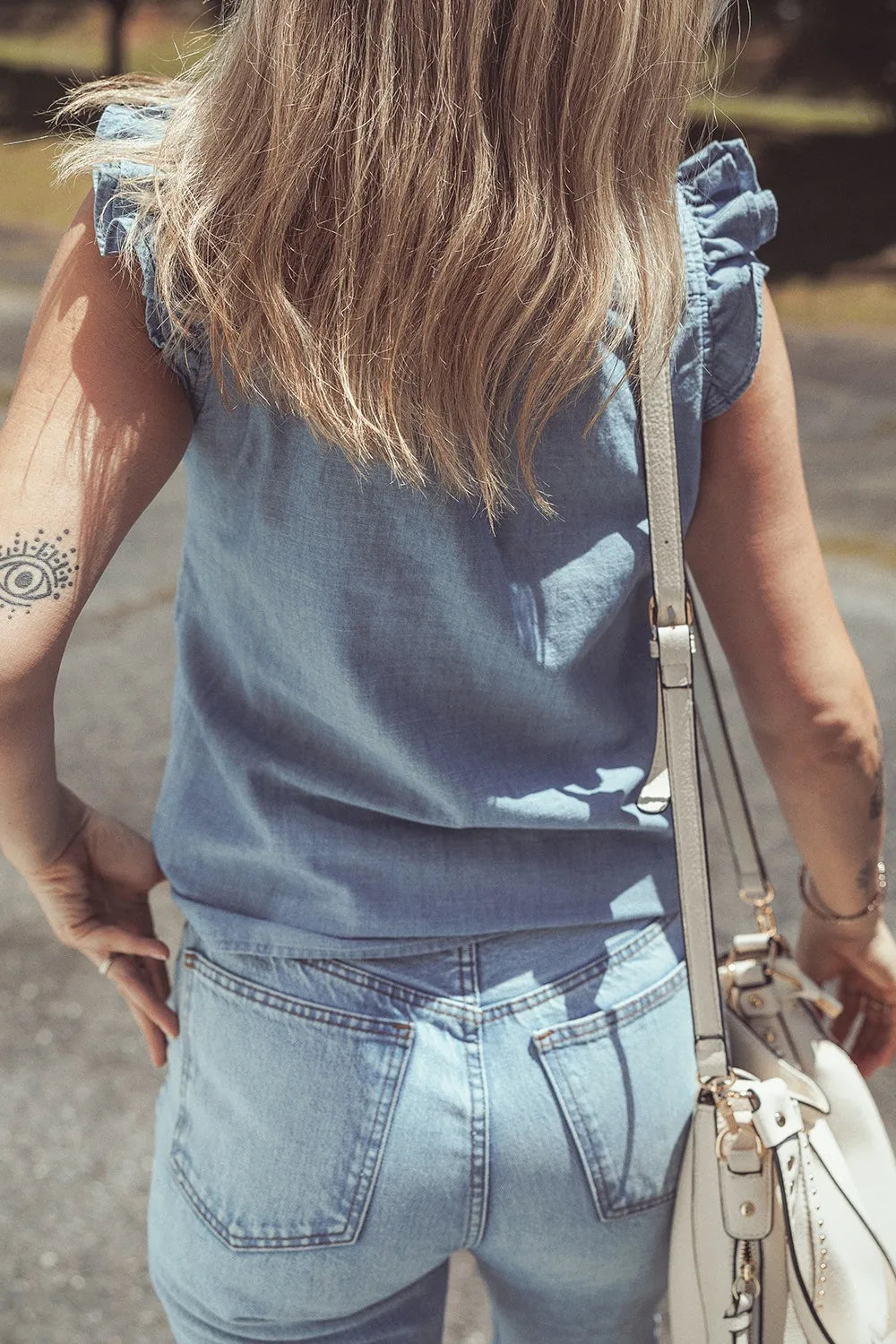 Chambray sleeveless blouse with ruffle trim and a white crossbody bag.