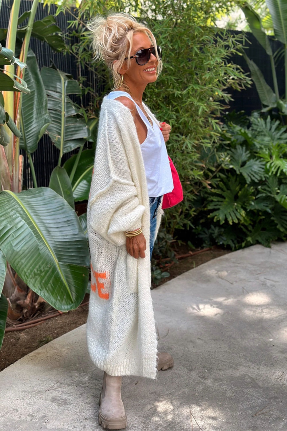 White knit maxi cardigan with orange peace sign graphic, long sleeves, open front.