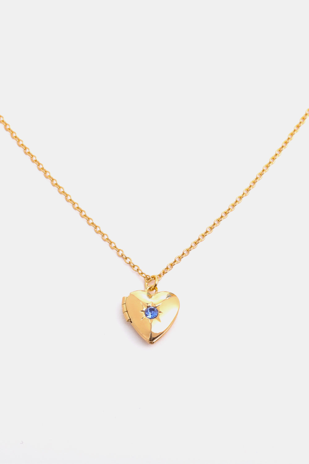 Gold heart locket necklace with blue gemstone and starburst detail on a delicate chain.