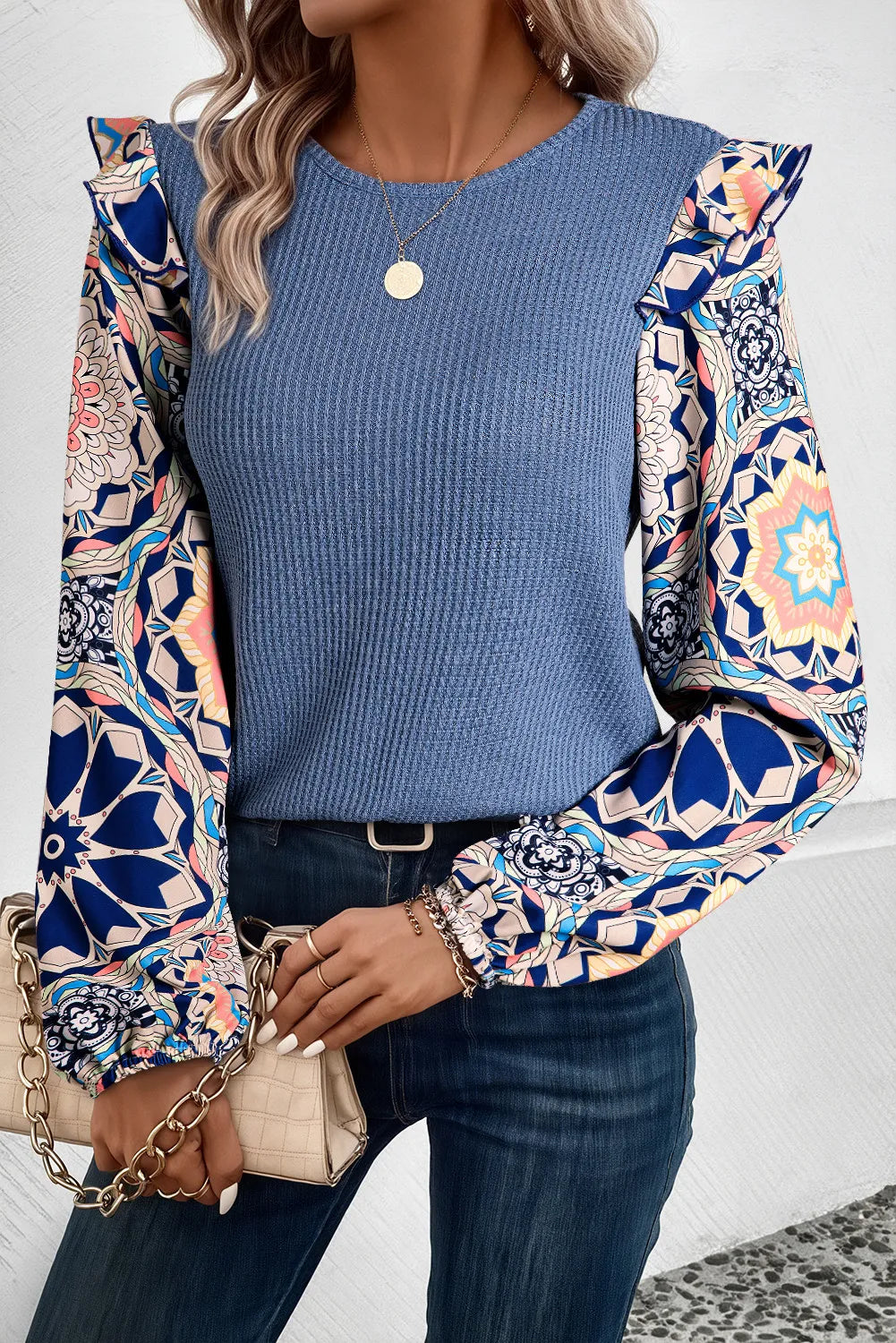 Dusty blue knit top with ruffled printed sleeves and a round neckline.