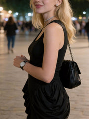 Black ruched midi dress with slit, sleeveless, draped detail, worn with a watch and handbag.