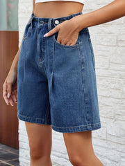 Pleated denim bermuda shorts in medium wash with button closure and front pockets.