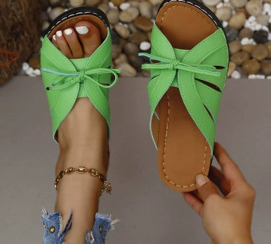 Green criss-cross wedge sandals with bow detail and brown sole.