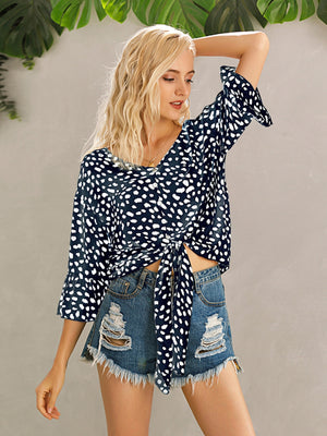 Dark blue spotted knot-front blouse with flared sleeves and tie detail.