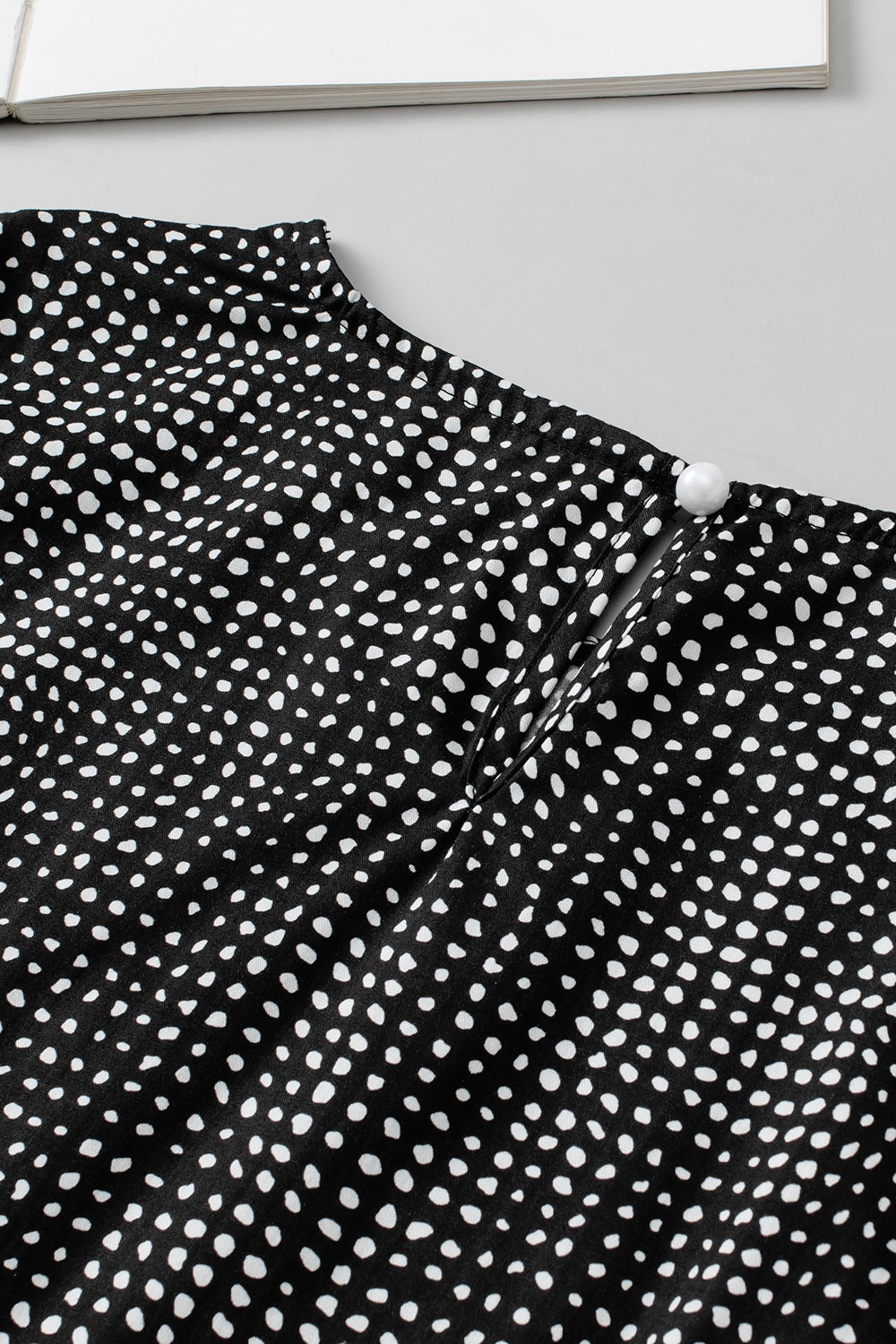 Black dotted blouse with puff sleeves and pearl button detail at the neckline.