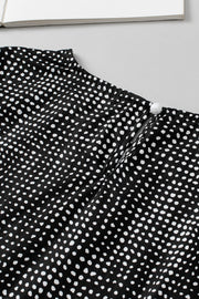 Black dotted blouse with puff sleeves and pearl button detail at the neckline.