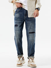 Men's dark blue distressed cotton jeans with patchwork details and cuffed hems.