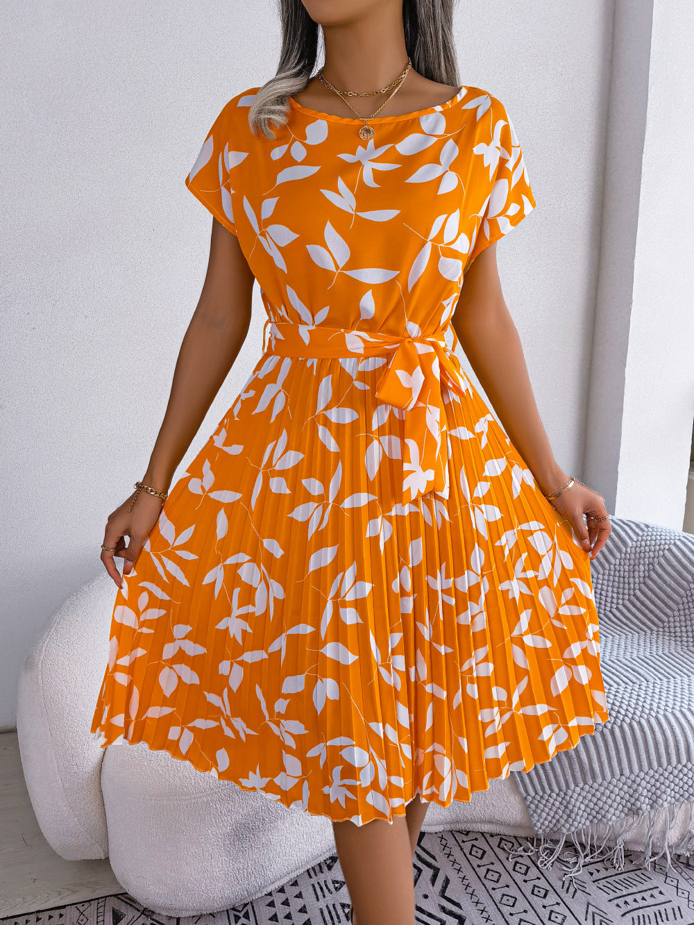 Orange midi dress with white leaf print, short sleeves, belted waist, and pleated skirt.